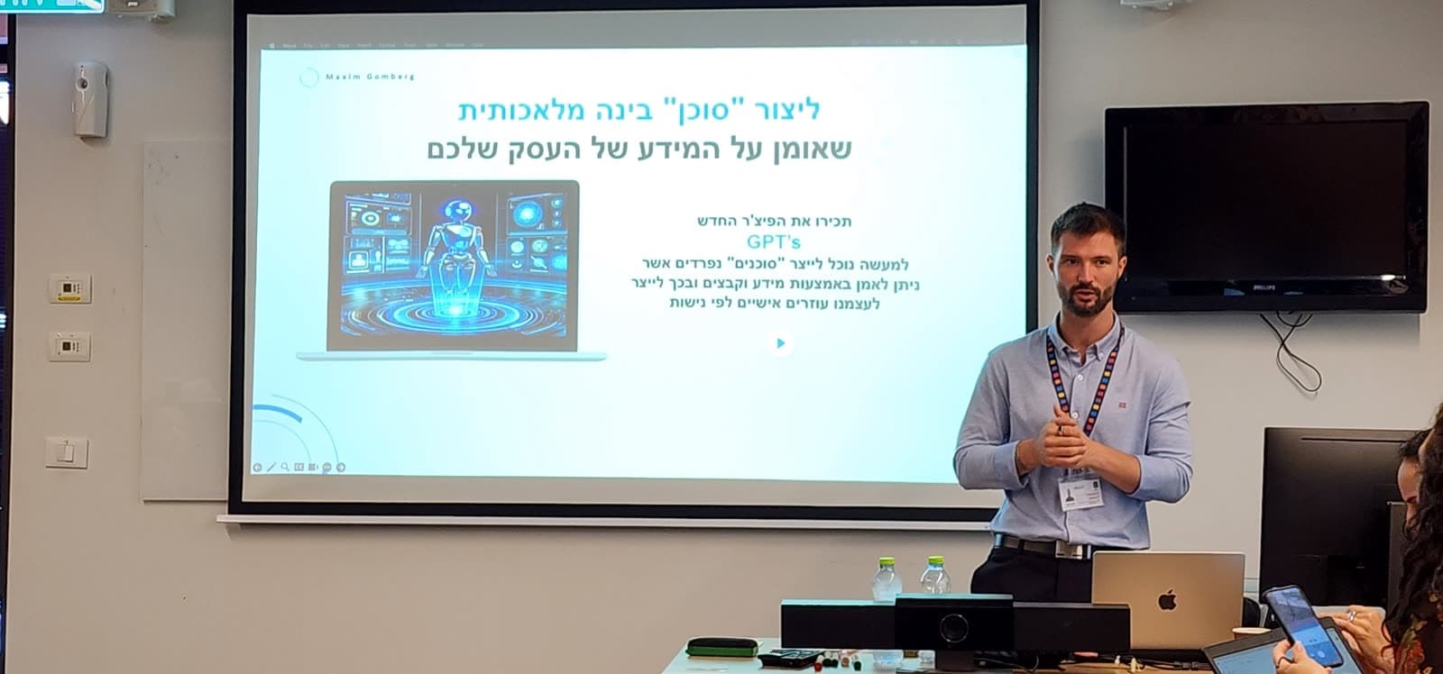מקסים גומברג בסדנת סוכני AI בארגון, מול מסך שכתוב עליו ״ליצור ׳סוכן׳ בינה מלאכותית שאומן על המידע של העסק שלכם״