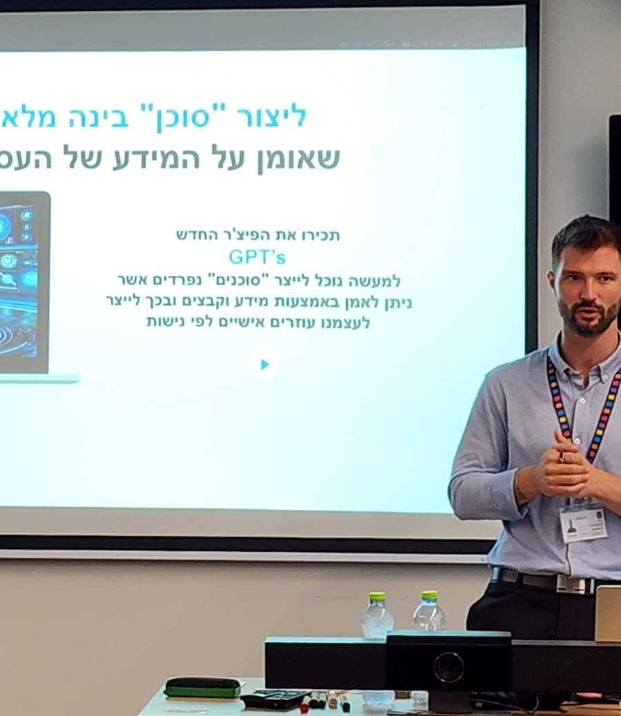 מקסים גומברג בסדנת סוכני AI בארגון, מול מסך שכתוב עליו ״ליצור ׳סוכן׳ בינה מלאכותית שאומן על המידע של העסק״