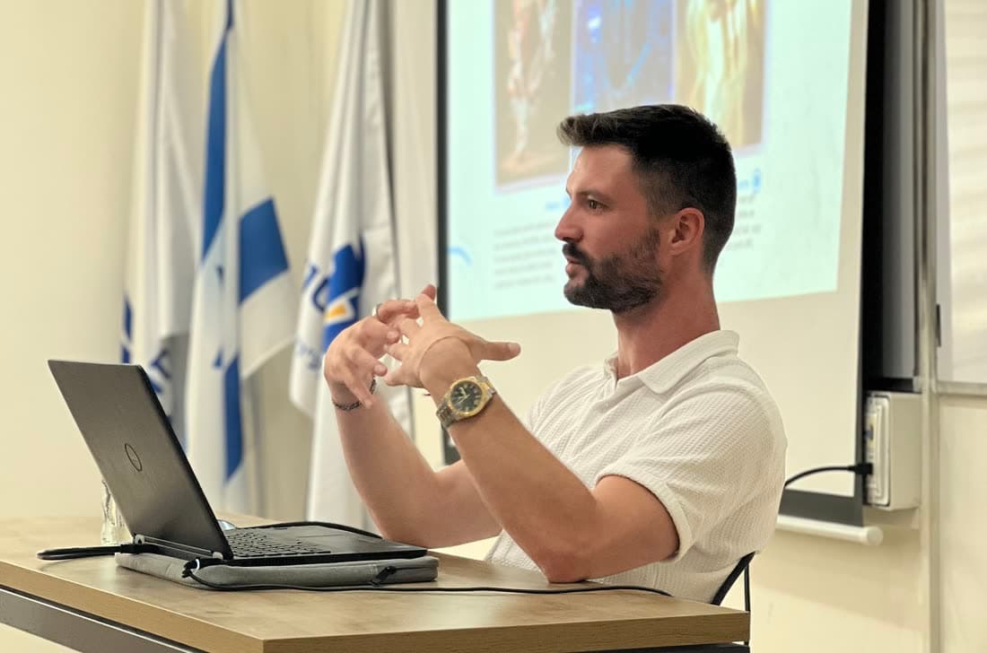 מקסים גומברג מדגים מהמחשב בחדר הדרכה, מול מסך מוקרן