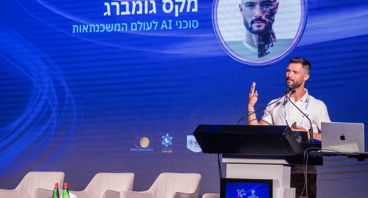 מקסים גומברג בפודיום ועידת המשכנתאות, שמו ותפקידו על המסך שמאחוריו